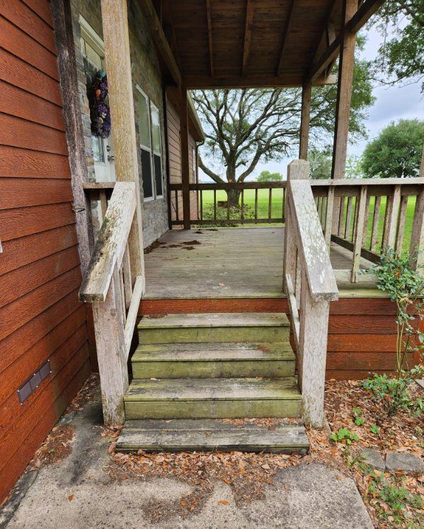 Before house washing services, showing a weathered porch with dirty wooden steps, handrails, and floor, with visible moss and dirt buildup.