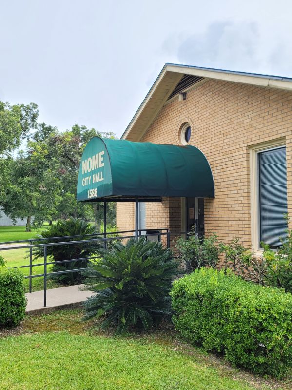 Cleaned and refreshed awning at Nome City Hall, with the rust and stains removed, restoring the original green fabric. The surrounding area remains unchanged, with cleaning tools in place.