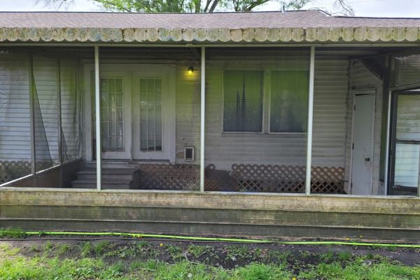The exterior of a house with a dirty porch and weathered siding, showing signs of wear before house washing services.
