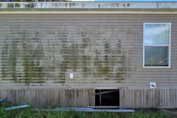 The exterior of a house with visible dirt and mildew stains on the siding, showing the need for washing services.