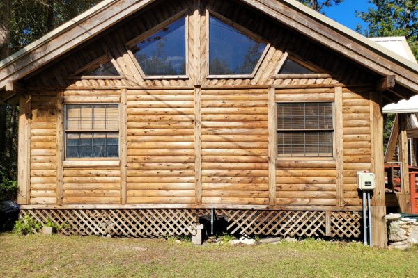 The exterior of a wooden house showing clean logs and windows with a refreshed appearance after house washing services.