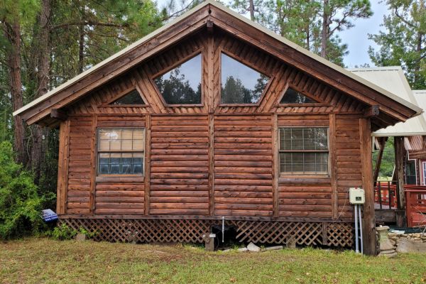The exterior of a wooden house with darker, weathered logs and visible dirt, shown before house washing services.