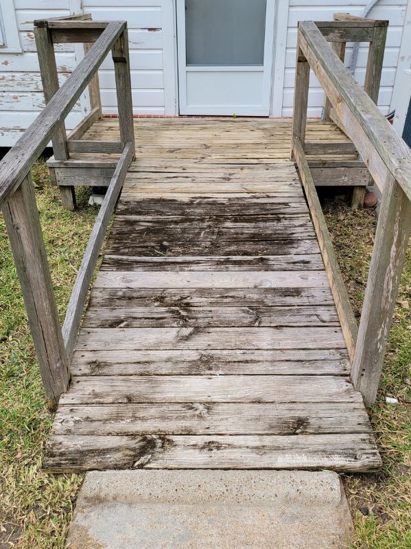 Weathered and stained wooden ramp showing dark spots and peeling paint on the boards and railing, indicating signs of aging and exposure to the elements.