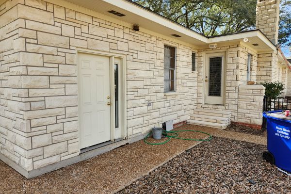 The same exterior of the house with the stone surface looking much cleaner and brighter, with the ground cleared of leaves and dirt, presenting a well-maintained appearance.