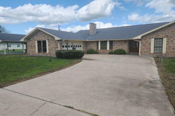 The driveway of a house with a freshly cleaned, smooth, and uniform surface, free from stains and dirt, revealing a much neater appearance with clear distinctions from the surrounding lawn.