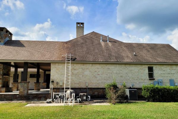 A rear view of a residential building with brick siding and outdoor equipment, ideal for demonstrating house washing services to clean and maintain exterior surfaces.
