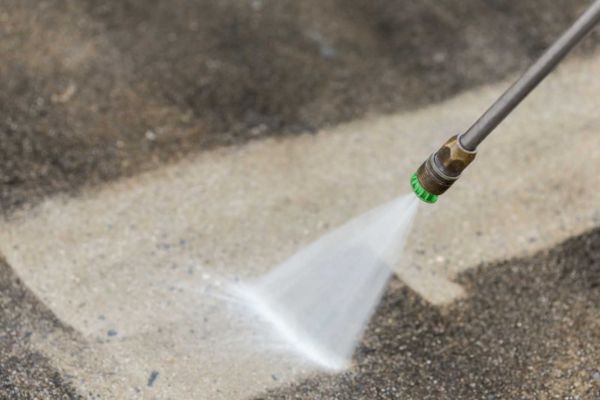 A close-up of a pressure washer nozzle spraying water on a concrete surface, part of concrete washing services, effectively cleaning the grime and dirt off the surface.