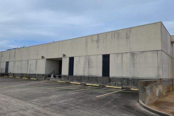 Before Washing Services: A beige warehouse building with visible dirt and stains on the walls. The concrete base and parking lot are shown, with several empty spaces in front of the building. The windows are covered with black grilles.