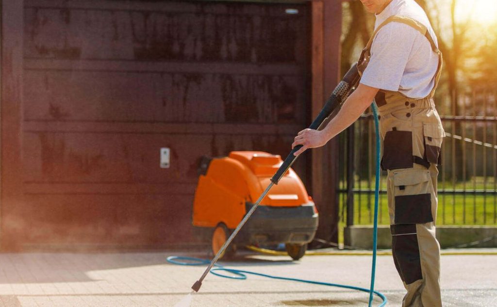 A person using a high-pressure washer to clean a paved surface, with a powerful pressure washing machine in the background. The scene captures the effectiveness and precision of professional cleaning services. Best Pressure Washing Services ensure a spotless and refreshed exterior for any property.