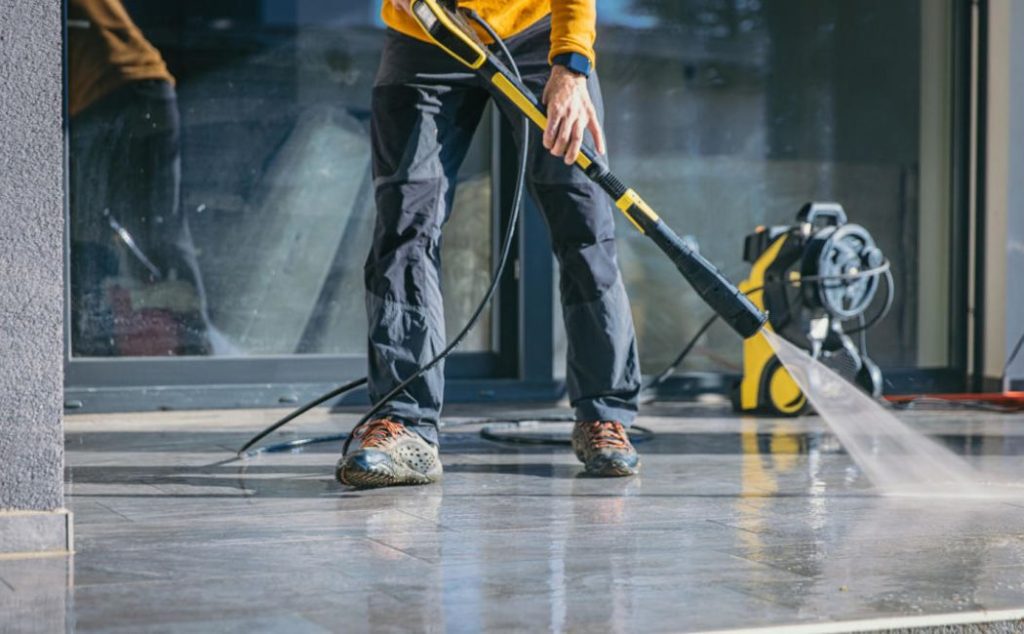 A person is using a pressure washer to clean a paved surface outside a building. The professional is focused on the task, ensuring the area is spotless. This image showcases the power and efficiency of pressure washing services in maintaining clean, attractive outdoor spaces.