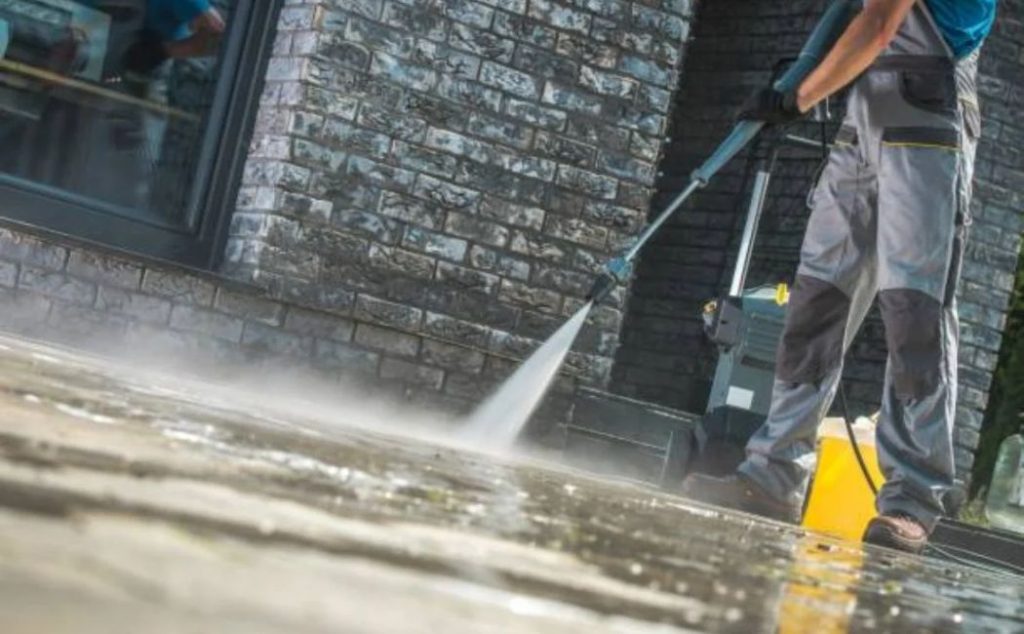 A professional using a pressure washer to clean a stone pathway in front of a building. The high-powered water stream is effectively removing dirt and grime from the surface, showcasing the efficiency of Pressure Washing Services in maintaining clean and well-kept exteriors.