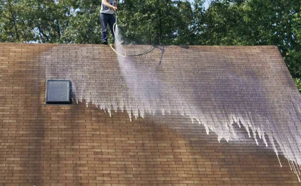 Roof washing services professional spraying cleaning solution on a shingle roof to remove dirt, algae, and stains effectively.