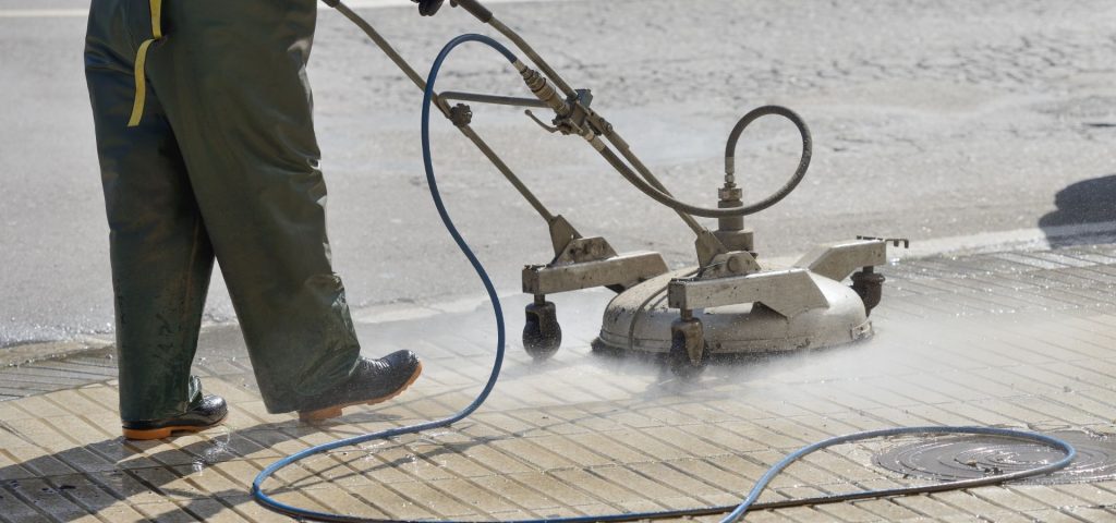 A technician is using a commercial pressure washer with a surface cleaner attachment to wash a concrete surface. The cleaning process removes dirt, stains, and debris, ensuring a well-maintained appearance. This is an example of concrete washing services designed to enhance the cleanliness and durability of concrete surfaces.
