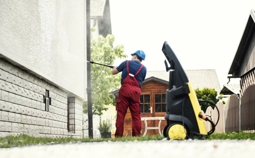 Soft washing services in action, with a professional gently cleaning a home's exterior walls using specialized low-pressure equipment.