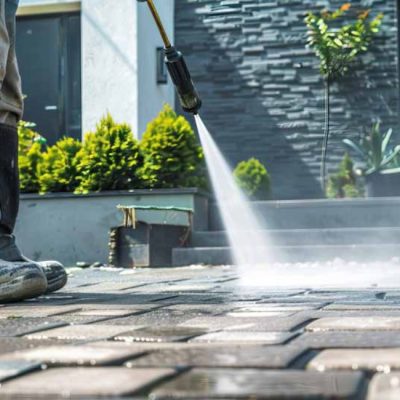 Worker using professional equipment for soft washing outdoor stone pavers, removing dirt and buildup to restore a clean surface.