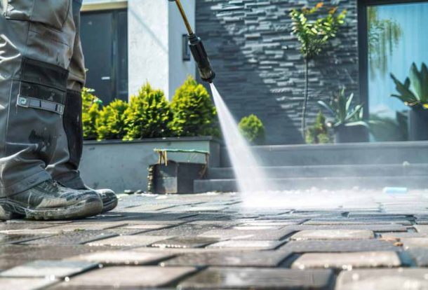 Worker using professional equipment for soft washing outdoor stone pavers, removing dirt and buildup to restore a clean surface.