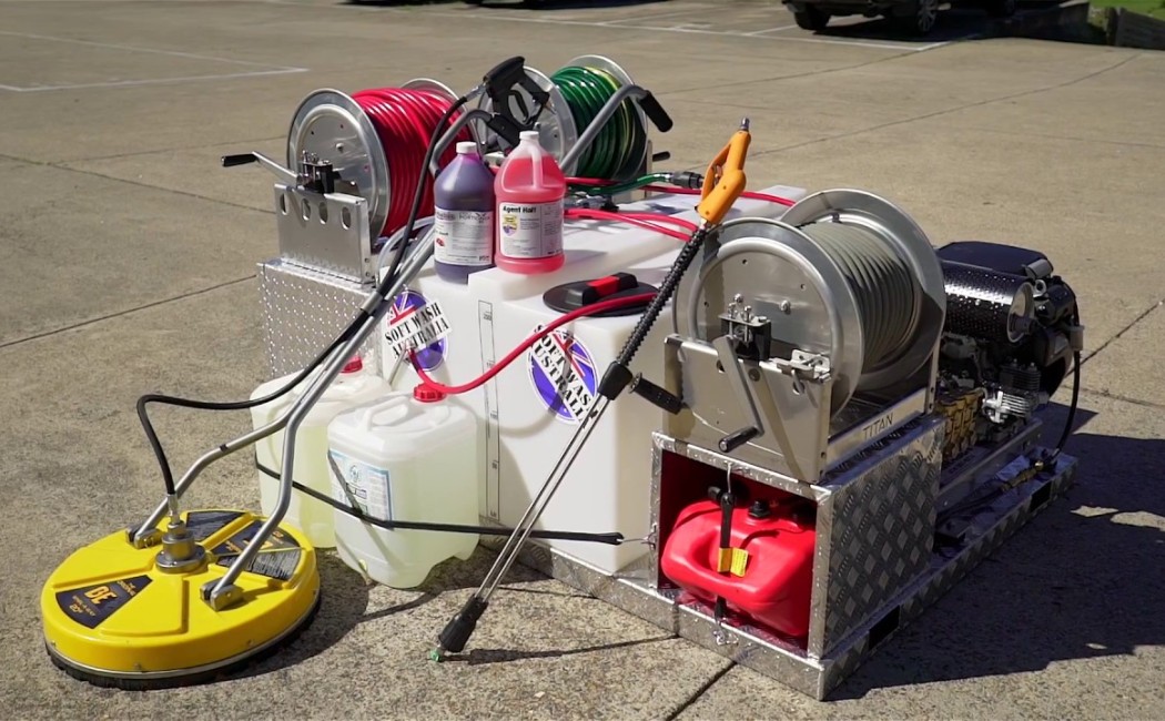 Commercial-grade soft wash equipment and solutions setup featuring hose reels, chemical tanks, a surface cleaner, and a pressure washing unit arranged on a concrete surface.