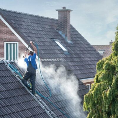 A professional from a roof washing company uses a high-pressure hose to clean the roof of a residential home.