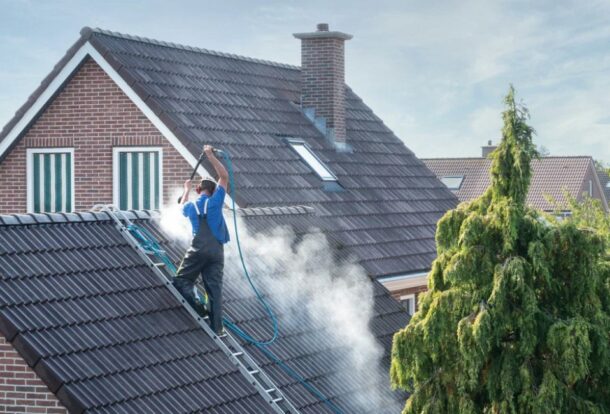A professional from a roof washing company uses a high-pressure hose to clean the roof of a residential home.