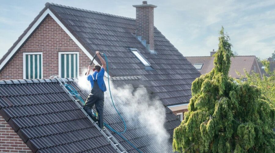 A professional from a roof washing company uses a high-pressure hose to clean the roof of a residential home.