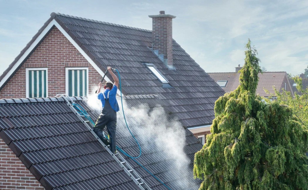 A professional from a roof washing company uses a high-pressure hose to clean the roof of a residential home.