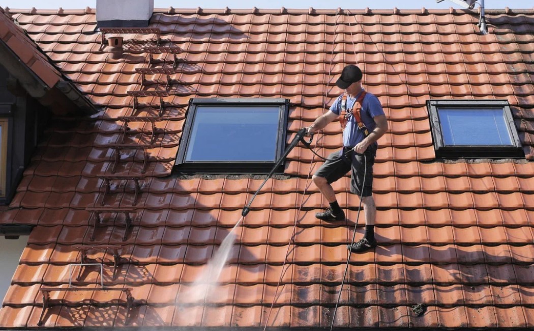 A professional from a roof washing company uses a pressure washer to clean a tiled roof, ensuring it is free from dirt and debris.