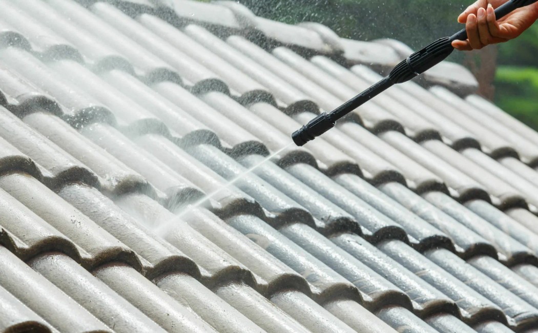 A roof washing company technician uses a high-pressure washer to clean dirt and grime from tiled roofing.