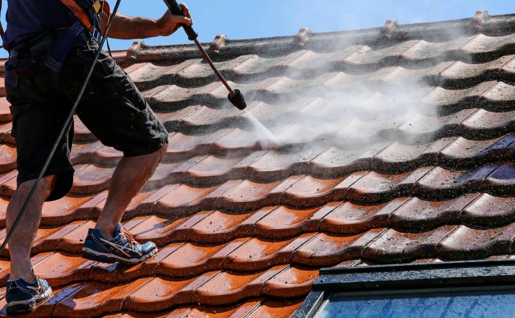 A professional from a roof washing company is cleaning roof tiles with a pressure washer, removing dirt and debris.